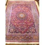 AN EARLY 20TH CENTURY KIRMAN/WOOLLEN CARPET, claret ground with multi strap border, foliate designs,