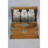 A LATE VICTORIAN OAK TANTALUS, with silver plated mounts, fitted with a set of three decanters,