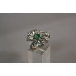 A MODERN EMERALD AND DIAMOND FANCY BOW DESIGN RING, one oval mixed cut emerald measuring