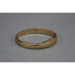 A LATE 20TH CENTURY 9CT GOLD OVAL HINGED BANGLE, half engraved in a fancy scroll design, measuring