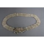 A PERSIAN WHITE METAL FILIGREE WORK BELT, the clasp of bow form with three droppers suspended from