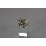 A MODERN EMERALD AND DIAMOND FANCY BOW DESIGN RING, one oval mixed cut emerald measuring