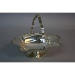 AN EDWARDIAN SILVER SWING HANDLED CAKE BASKET, of oval shaped form, wavy handle, part reeded rim, on