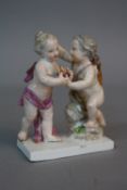 A 19TH CENTURY MEISSEN FIGURE GROUP OF A CHERUB OR CUPID, giving a flaming torch to a putto, on a
