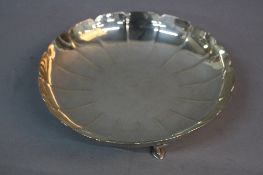 AN ELIZABETH II CIRCULAR SILVER DISH, wavy rim with embossed lines, on four short cabriole legs with