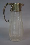AN EDWARDIAN SILVER MOUNTED CUT AND ETCHED GLASS CLARET JUG, the hinged cover engraved with