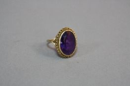 A LATE 20TH CENTURY 9CT GOLD LARGE AMETHYST SINGLE STONE RING rub over set in a twist rope edge,