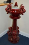 A VICTORIAN STYLE JARDINIERE ON STAND, with claret glaze, moulded with three mythical beasts handles