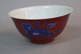 A CHINESE PORCELAIN BOWL, the iron red ground decorated with dragon dogs and flaming pearls, blue