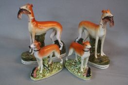 TWO PAIRS OF LATE VICTORIAN STAFFORDSHIRE POTTERY GREYHOUNDS, one pair carrying hares in their