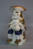 AN EARLY 19TH CENTURY PEARLWARE TOBY JUG, modelled as seated holding foaming quart, chipped