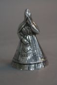 A CONTINENTAL WHITE METAL TABLE BELL, in the form of a lady, her head wrapped in a shawl and holding
