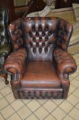 A BROWN LEATHER BUTTONED WING BACK ARMCHAIR (sd)