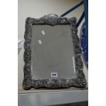 A REPRODUCTION EASEL BACK MIRROR IN AN ORNATELY CAST SILVER PLATED FRAME