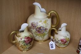 THREE ROYAL WORCESTER BLUSH IVORY FLAT BACKED JUGS, each florally decorated, gilding to handles