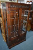 AN OLD CHARM OAK LEAD GLAZED TWO DOOR CHINA CABINET, above a double door cupboard base,