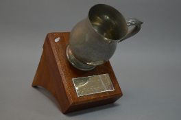 A PRESENTATION PEWTER DRINKING MUG, attached to a wooden bracket plinth, commemorating the Rev
