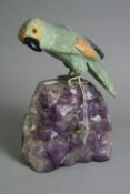 A CARVED ORIENTAL HARDSTONE PARROT, mounted on an amethyst geode, height approximately 23.5cm (