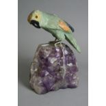 A CARVED ORIENTAL HARDSTONE PARROT, mounted on an amethyst geode, height approximately 23.5cm (