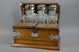 A LATE VICTORIAN OAK TANTALUS WITH SILVER PLATED MOUNTS, mirror back, fitted with three square glass