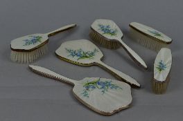 AN ELIZABETH II SILVER AND WHITE ENAMEL SIX PIECE DRESSING TABLE SET, decorated with a spray of