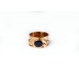 A wide yellow metal ring, unmarked, collet set with central oval cut sapphire coloured stone,