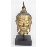 A gilt wooden Buddha's head, late 20th/early 21st century, on ebonized base, 68cm high Note: this