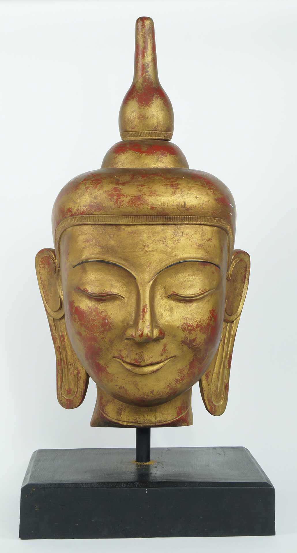 A gilt wooden Buddha's head, late 20th/early 21st century, on ebonized base, 71cm high Note: There