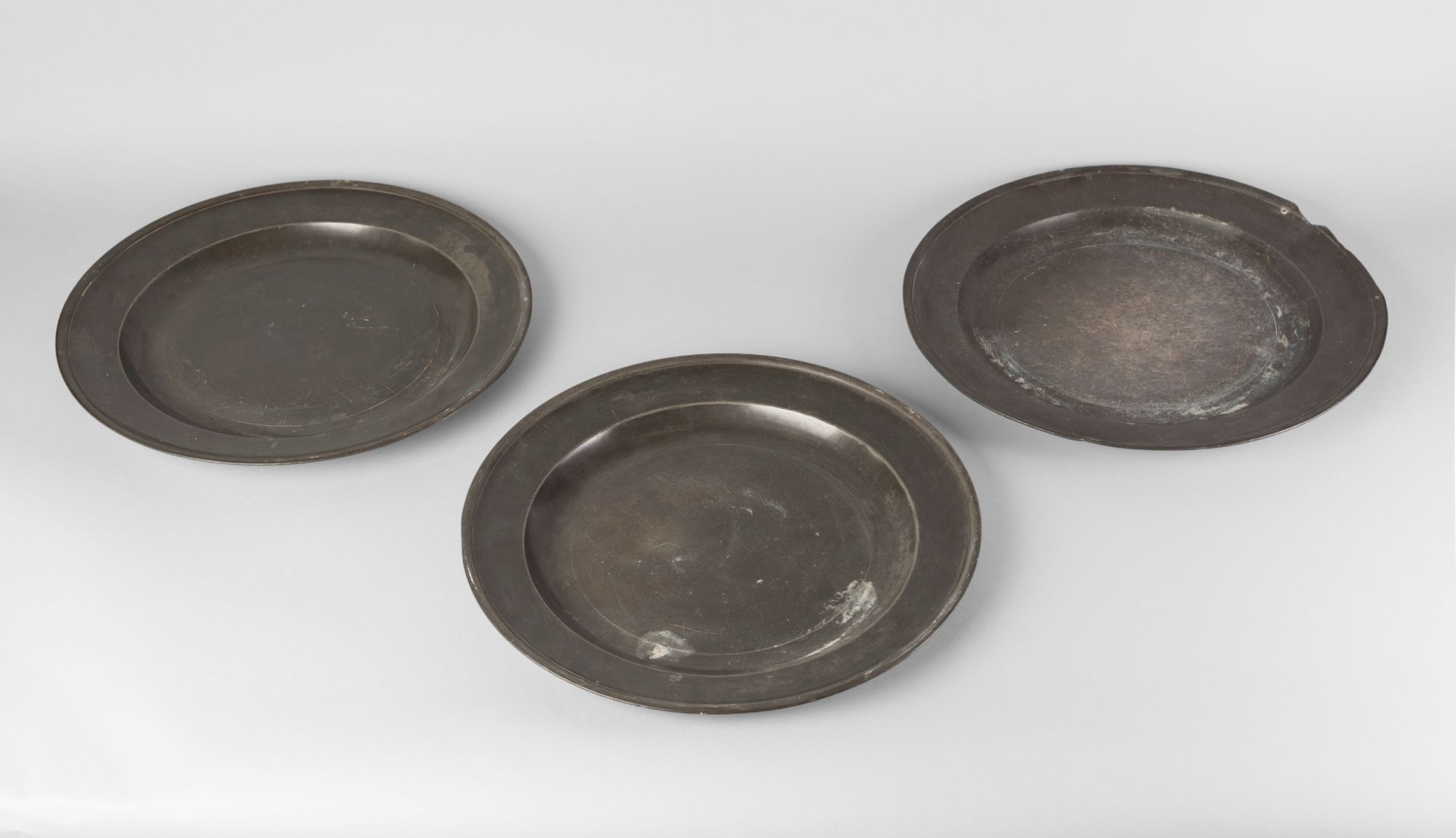 A set of four pewter chargers, 18th century, with plain reeded rims, all bearing faint touch marks,