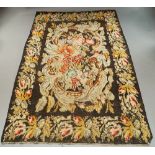 A flat weave rug with scroll edge panel of roses on charcoal field with foliate and rose border,