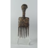 A Tribal hardwood comb, late 19th/20th century, the handle in the form of a face with neck rings,