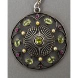 An unmarked 14 ct white gold pendant Of pierced circular form set with peridots, pearls and rubies,