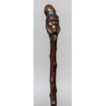 A Victorian single piece carved wooden walking stick The handle formed as a gentleman wearing a top