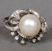 A 14K white gold pearl and diamond ring Of pierced scrolling floral form. 2.5 cm wide.