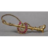 An unmarked gold ruby set bar brooch formed as riding crop and horseshoe 5.5 cm wide.