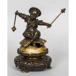 A bronze cast table bell Modelled as an Eastern child striking a bell upon which he is seated,