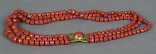 An Italian 9 ct gold mounted three strand coral necklace The beads facet cut. 65 cm long overall.