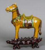 A Chinese Tang style pottery model of a horse Mounted on a finely carved hardwood plinth base.