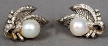 A pair of 14K white gold pearl and diamond ear clips Each of pierced scrolling floral form.