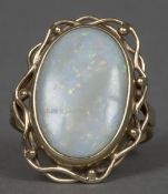 A 9 ct gold opal set ring The large white cabochon opal set in scrolling framework. 2.5 cm high.