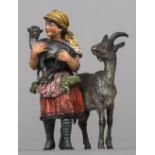 A cold painted bronze figural group Formed as a goatherdess carrying a baby goat,