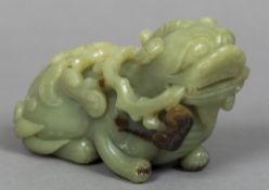 A Chinese carved green and russet jade temple lion Modelled recumbent,