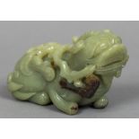 A Chinese carved green and russet jade temple lion Modelled recumbent,