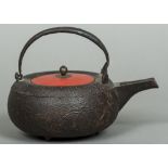 A Japanese cast iron teapot Cast with foliate sprays, the cover red lacquered. 15 cm high overall.