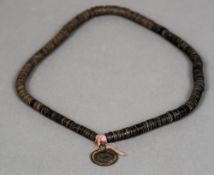 A tribal necklace Formed from small roundels, possibly coconut, set with a bronze pendant.