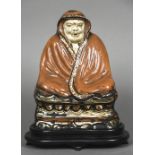 An antique Chinese pottery figure Modelled seated wrapped in a red ground robe,