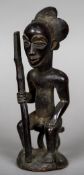 An African carved wooden tribal figure Modelled as a male seated holding a club. 28 cm high.