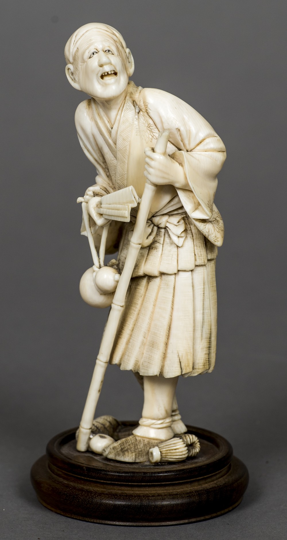 A 19th century Japanese ivory okimono Formed as a male figure holding a stick and a fan with a