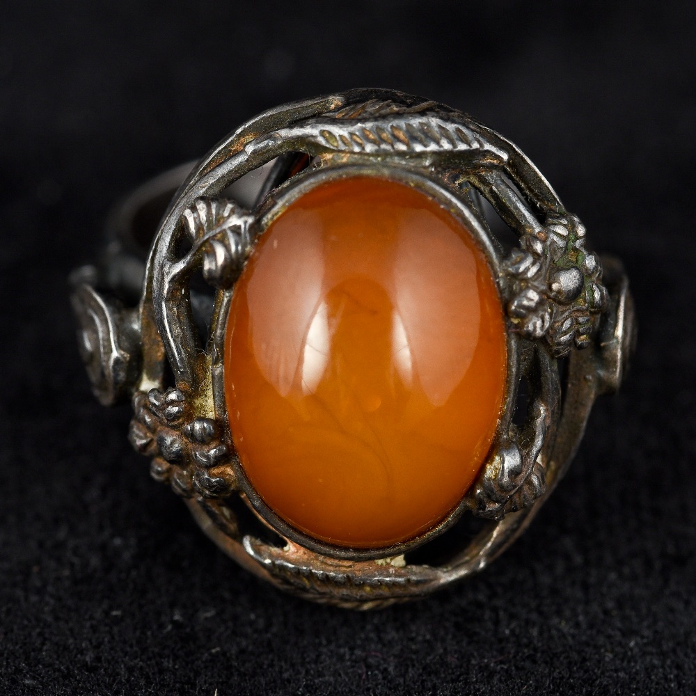 An Art Nouveau pierced silver ring The pierced floral bands centred with an amber cabochon.