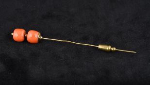 An unmarked gold coral bead mounted stick pin Set with two coral beads. 10.25 cm long.